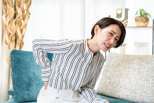 ソファに座って腰を押さえる女性