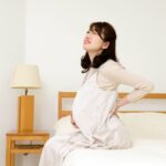 ベッドに腰かけて腰を押さえる女性