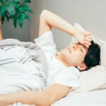 布団の中で額に手を当てる男性