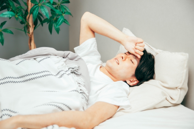 布団の中で額に手を当てる男性